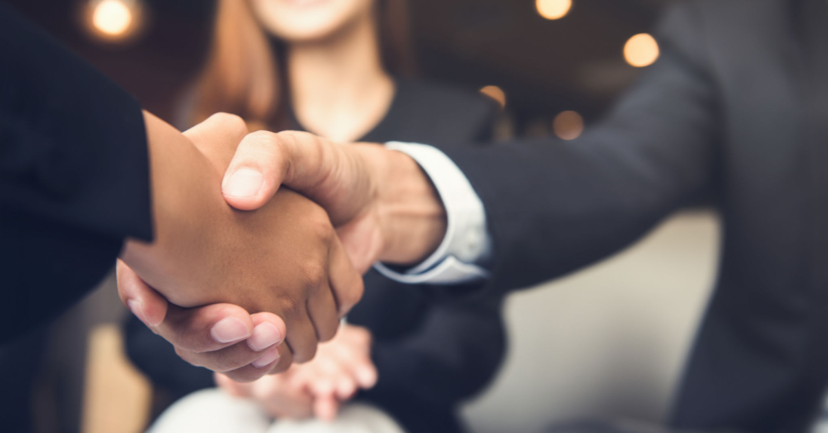 two business people shaking hands in front of an office.